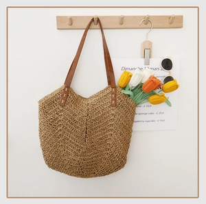 Détail du sac cabas en paille tissée avec anses en cuir marron et coutures en croix