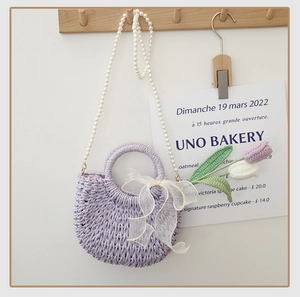 Detail of lilac woven straw bag featuring white lace bow and faux pearl chain strap
