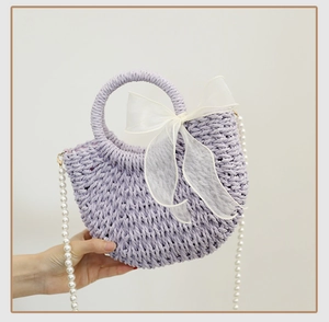Detail of lavender woven handbag featuring pearl strap and elegant white bow accent