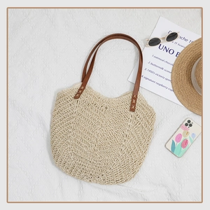 Détail d'un sac cabas en paille beige avec tissage en V et anses en cuir marron