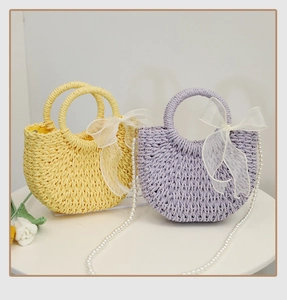Close-up of semi-circle straw bags with white organza bows and elegant pearl chain straps
