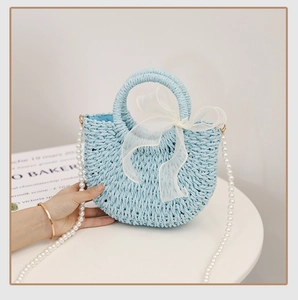 Detail of light blue straw bag with semi-transparent white bow and pearl shoulder strap