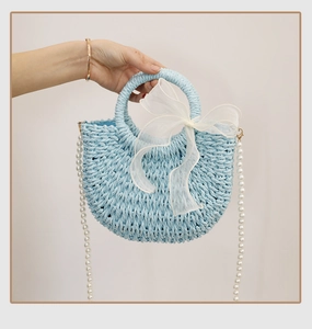 Detailed texture of blue woven straw bag with white organza bow and pearl strap