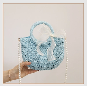 Detail of light blue straw bag featuring an organza bow and pearl chain strap