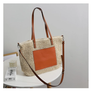 Detail of straw tote bag with brown leather pocket, handles and adjustable strap
