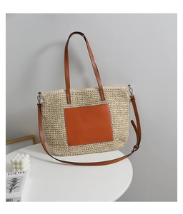 Close-up of woven straw tote bag featuring brown leather pocket and adjustable strap