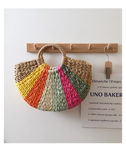 Detail of colorful rainbow straw tote bag featuring woven circular handles and beach style