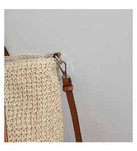 Detailed close-up of straw woven bag with brown leather strap and silver metal clasp