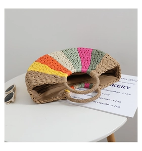 Detail of a semi-circular straw bag with rainbow stripes and round handles on a white table