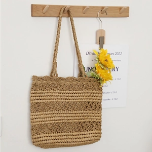 Hollow straw tote bag with sunflower decor on wooden hook against white wall background