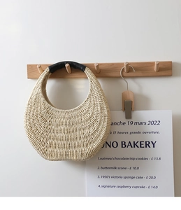 Detail of hand-woven straw bag featuring black leather handle on wooden wall hook