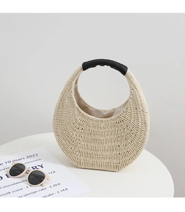 Detailed macro view of beige woven straw handbag with elegant black leather handle