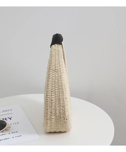 Detailed close-up of handmade straw woven bag with black leather handle and fine stitching