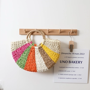 Rainbow striped semi-circle woven straw handbag hanging on a wooden hook for summer beach