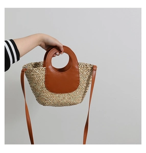 Detail of hand-woven straw bucket bag featuring premium brown leather handles and strap