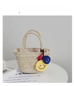 Dettaglio della borsa in paglia intrecciata con smiley in maglia e nappina rosa decorativa