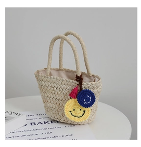 Dettaglio borsa in paglia intrecciata a mano con ciondoli smiley all'uncinetto e nappe