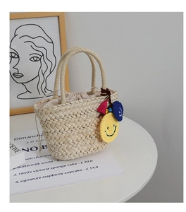 Dettaglio della borsa in paglia intrecciata con ciondolo smiley giallo e nappa rosa