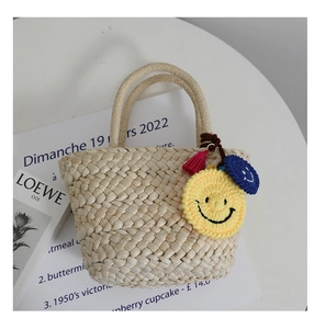 Dettaglio borsa a cesto in paglia intrecciata con ciondoli smile all'uncinetto e nappe