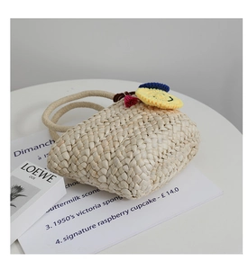 Dettaglio della borsa in paglia intrecciata a mano con charm smiley giallo e nappe rosse