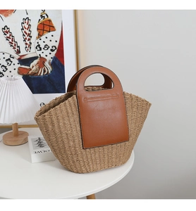 Close-up of woven straw tote bag with brown leather handles and decorative stitching