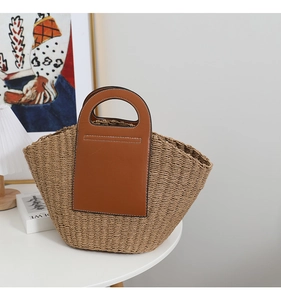 Detailed view of the woven straw tote bag featuring brown leather trim and white stitching