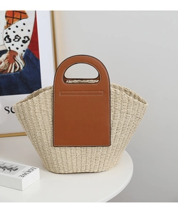 Close-up of woven straw handbag with brown leather handles and white contrast stitching