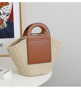 Close-up of woven straw basket bag with brown leather handles on a minimalist table