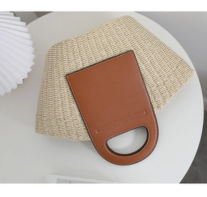 Detail of hand-woven straw bag with premium brown leather patchwork and circular handle