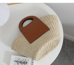 Detail of hand-woven straw tote bag with brown leather cutout handles and contrast stitching