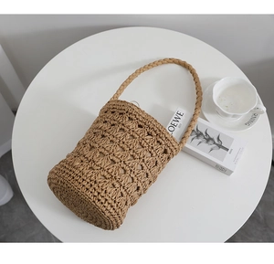 Détail du sac seau en paille tressée ajourée avec poignée tressée sur une table
