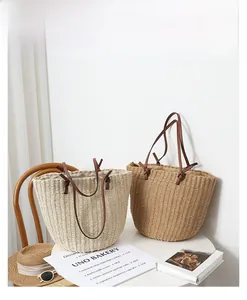 Detail of straw woven bucket bags with brown leather handles on a white table