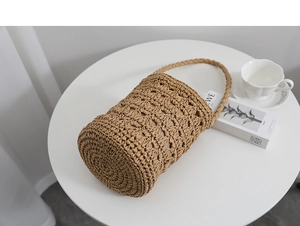 Gros plan détaillé d'un sac seau en paille tressée marron sur un décor de table minimaliste