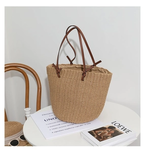 Detail of handwoven straw tote bag featuring brown leather straps and spacious interior