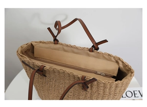 Detail view of woven straw tote bag featuring brown leather straps and zip closure