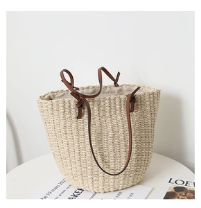 Close-up of beige woven straw tote bag with brown leather handles on white table