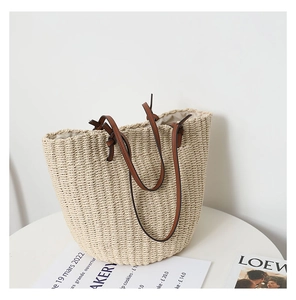 Detail of handwoven beige straw bucket bag with premium brown leather handles on a white table