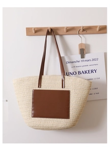 Detail of hand-woven straw tote bag with brown leather patch on a minimalist wall