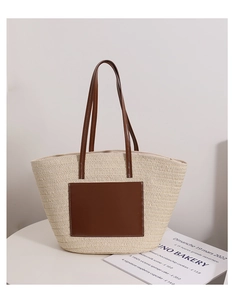 Close-up of woven straw tote bag featuring brown leather handles and reinforced stitching