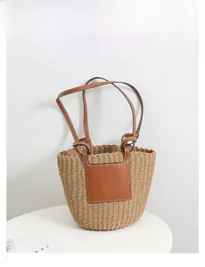 Detail of woven straw bucket bag with brown leather strap and decorative square on white base