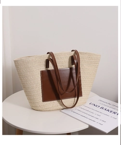 Detail of woven straw tote bag with brown leather pocket and handles on white table