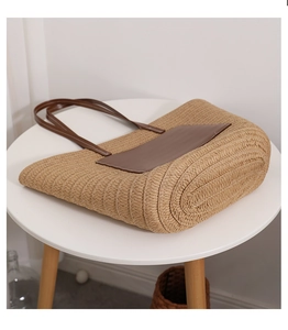 Detail of woven straw tote bag with brown leather pocket on a minimalist wooden table