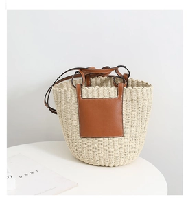 Detail view of woven straw bucket bag with brown leather handle on a white table
