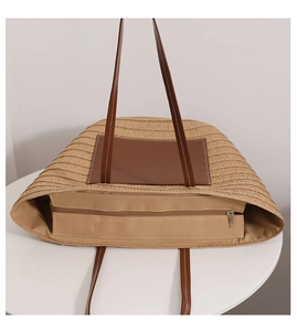 Close-up of woven straw tote bag featuring brown leather patch and zip closure detail