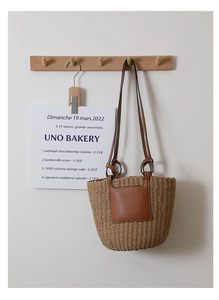 Detail of hand-woven straw shoulder bag featuring a brown leather pocket and long strap