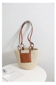 Detail of the woven straw bucket bag with brown leather handles and a square logo patch
