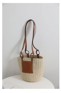 Close-up of a straw tote bag featuring a brown leather patch and long shoulder straps