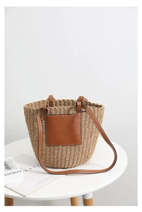 Close-up of handwoven straw bucket bag with brown leather patch and white stitching