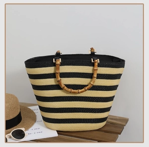 Detail of striped woven straw tote bag featuring authentic bamboo top handles for beach style
