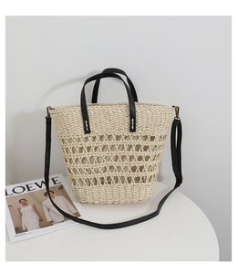 Detail of hollow-out straw tote with black leather straps on a minimalist white table